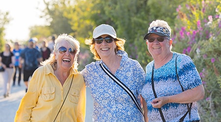 Three women posing for a photo on a busy walking path