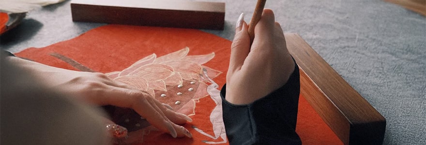 Close-up of a hand adding details to artwork on red fabric