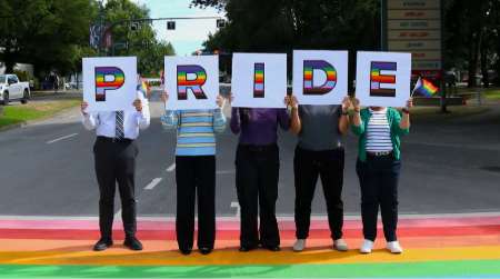 View of people on the rainbow crosswalk spelling out the word Pride on tiles